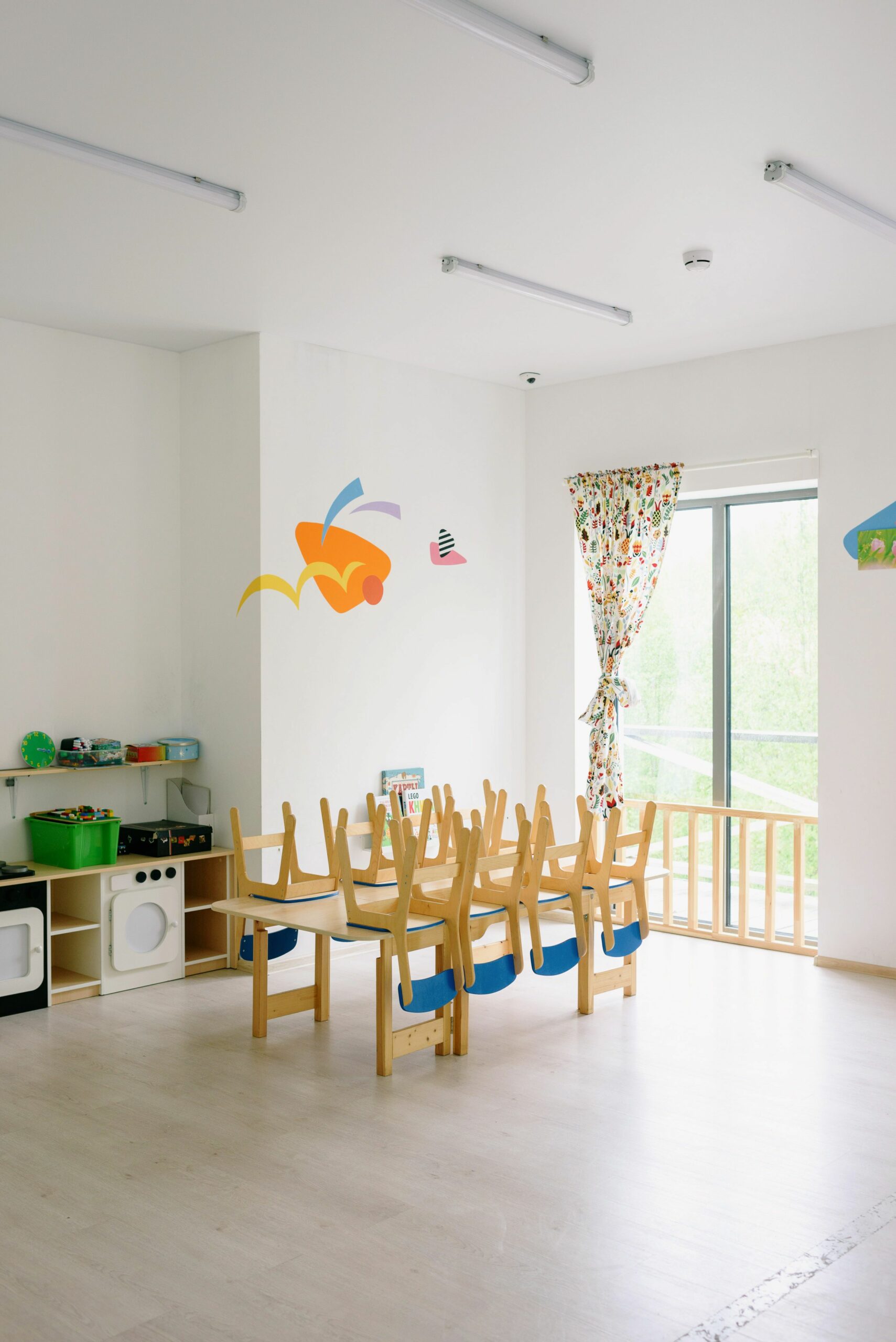 Spacious and bright kindergarten classroom with child-sized wooden furniture and playful decor.